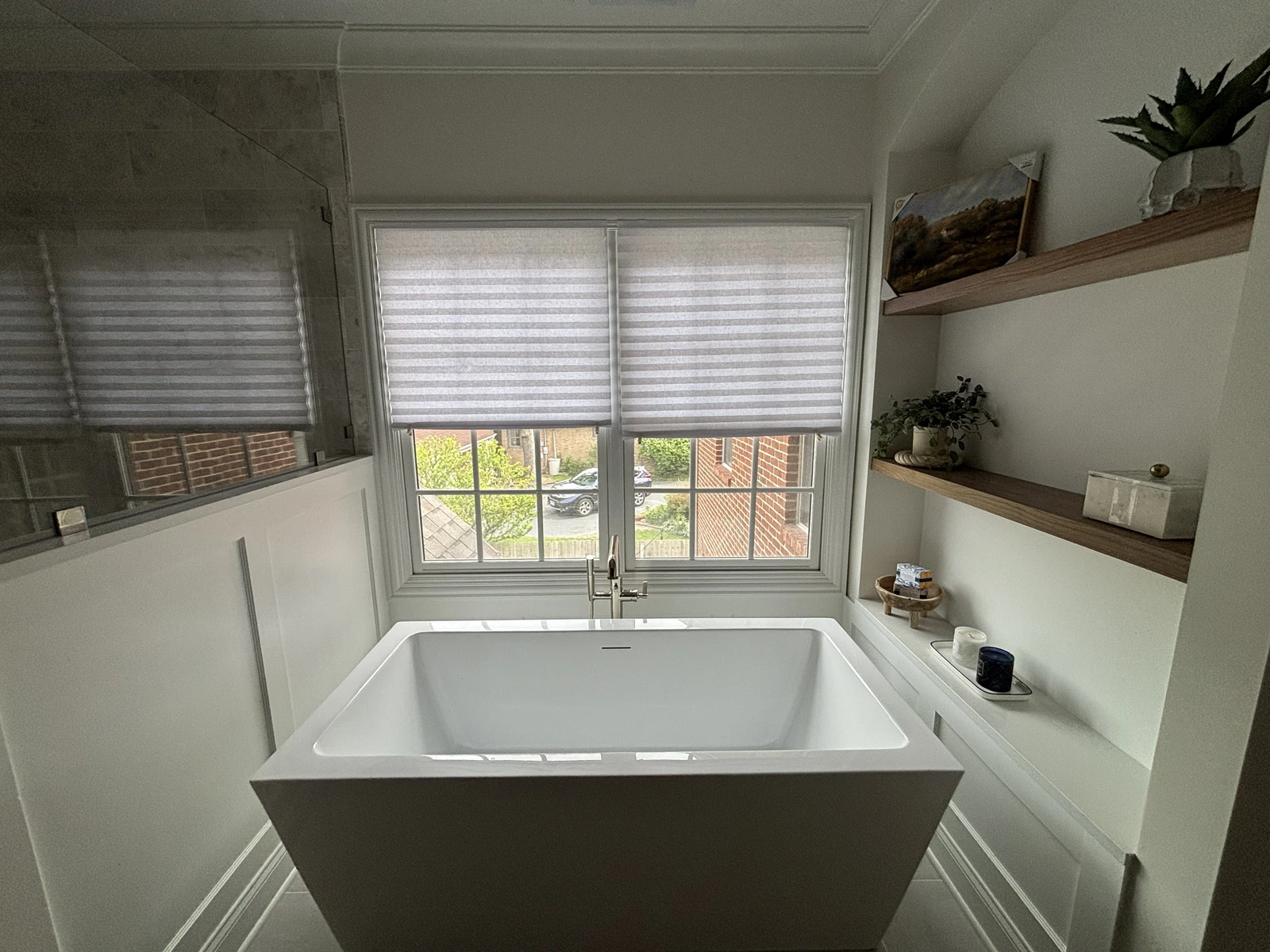 Freestanding bathtub beneath the windows with wood shelves and white wall trim