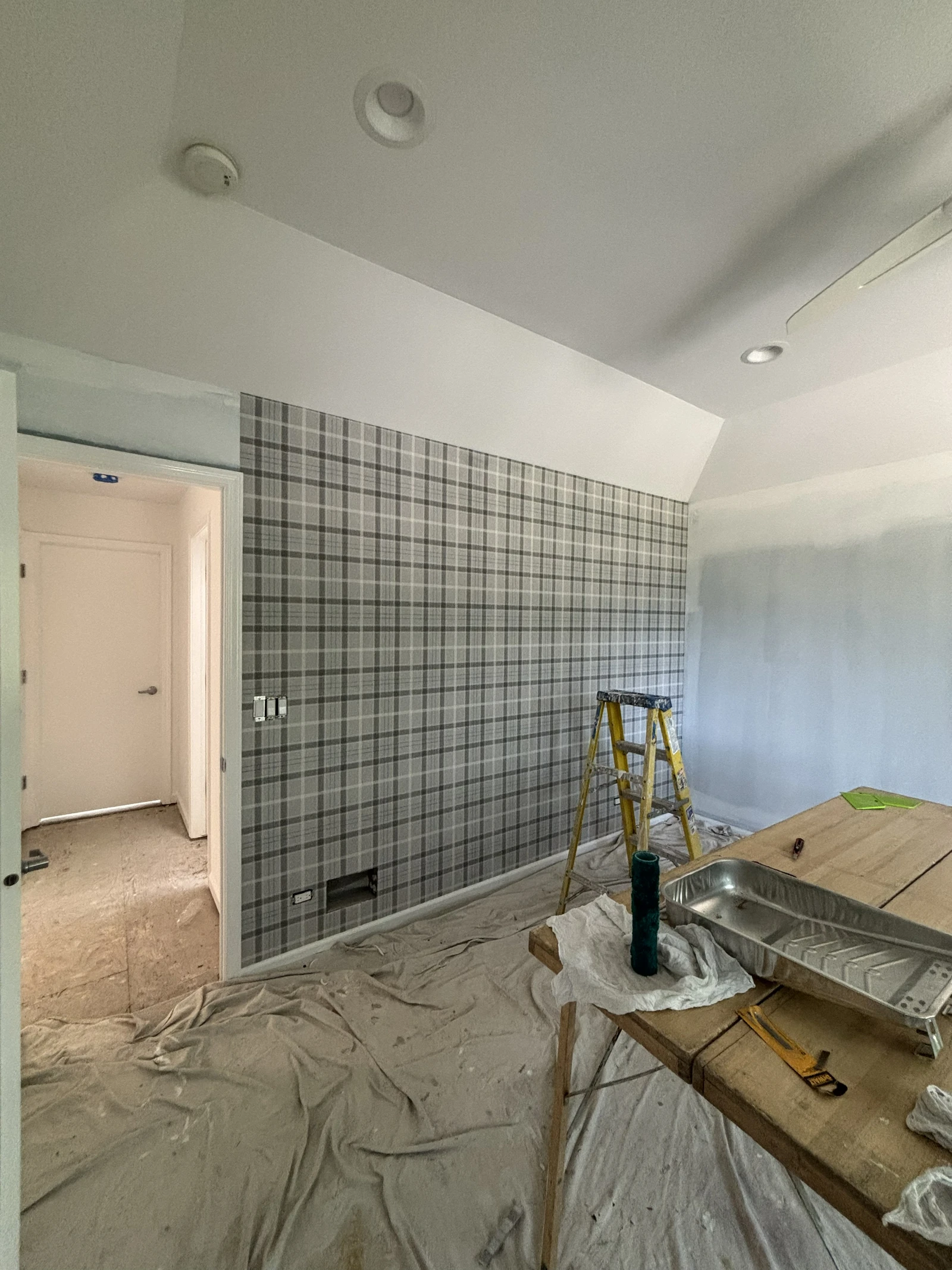 Plaid wallpaper accent wall during installation with the room protected for decorating